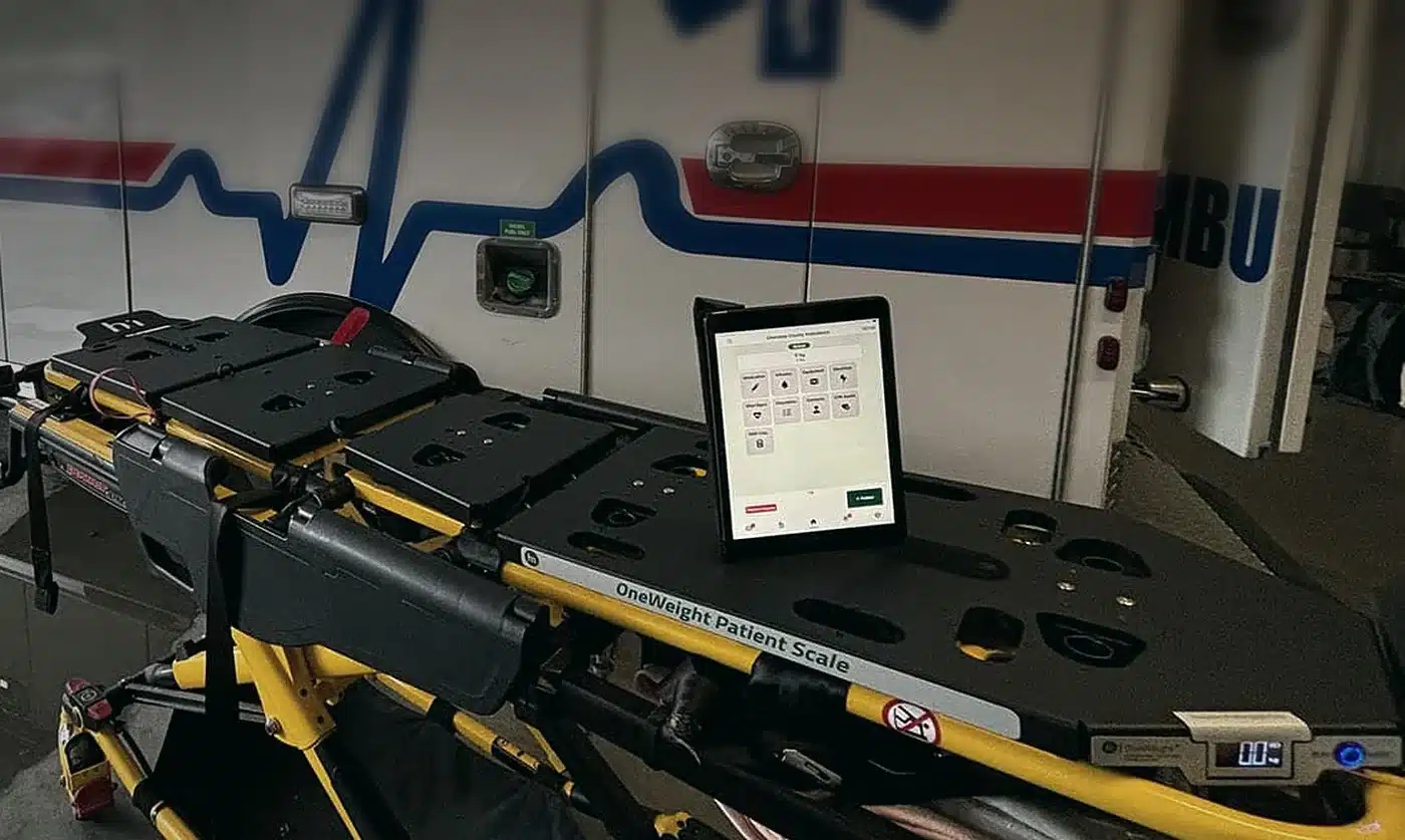OneWeight scale plates and side display on an ambulance cot, with the OneDose app on a tablet
